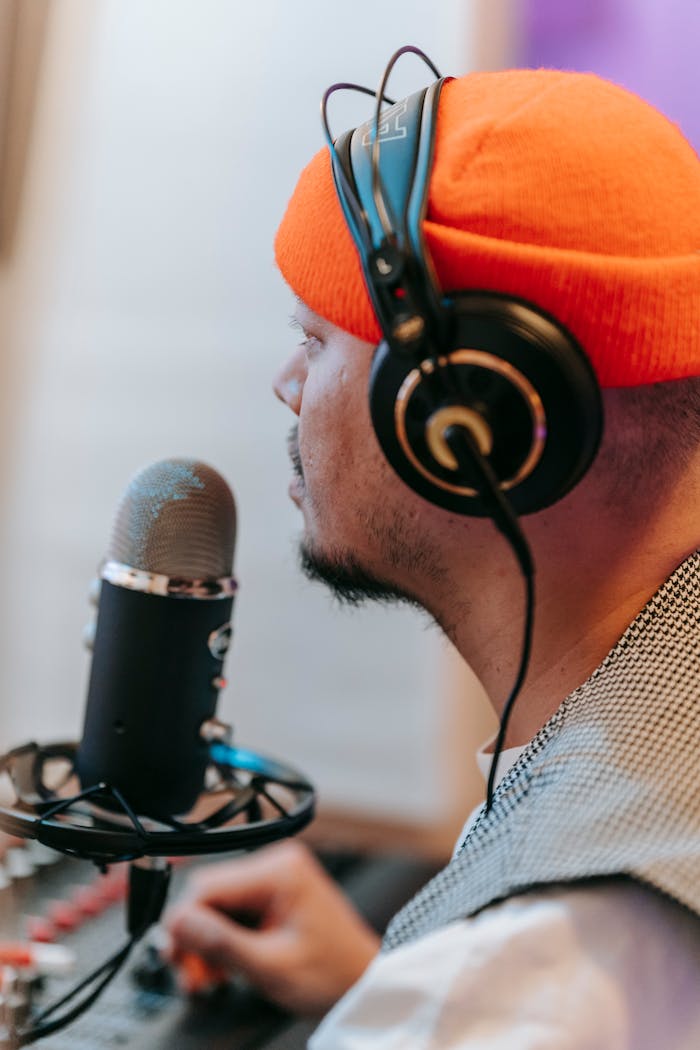 Man in orange hat using audio equipment and microphone for podcast in studio.